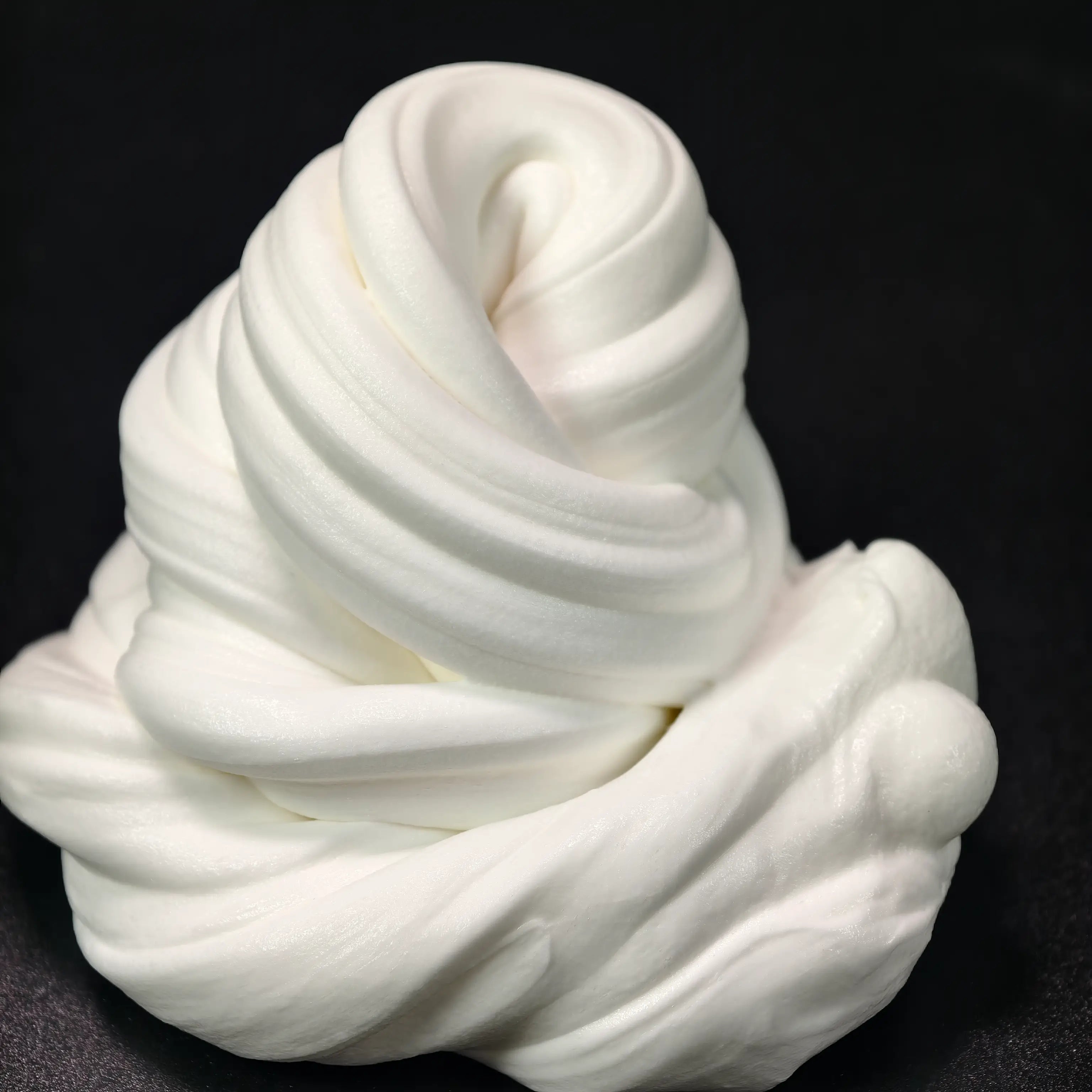 A mass of white, fluffy butter slime against a black background, demonstrating its soft and spongy texture.