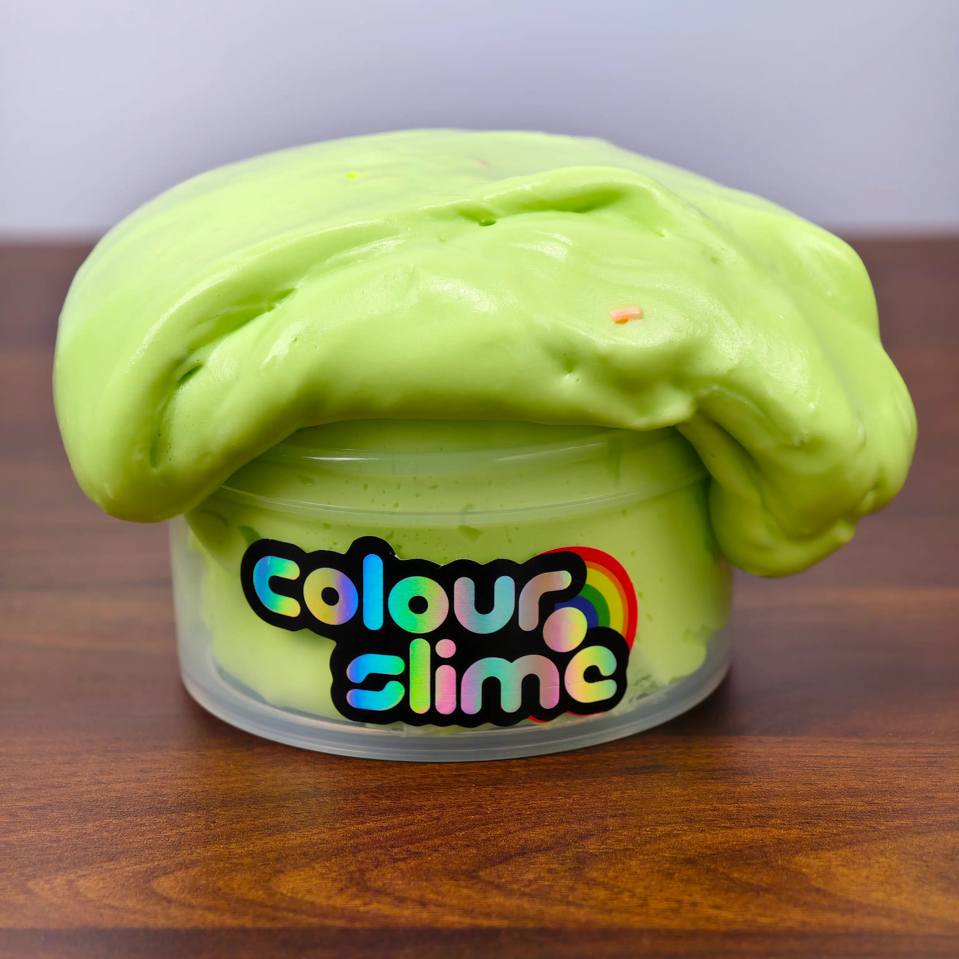 Green butter slime overflowing from a container labeled 'colour slime' on a wooden surface.
