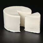 White creamy clay cheese wheel with a smooth, fine texture and a wedge cut out, set against a black background