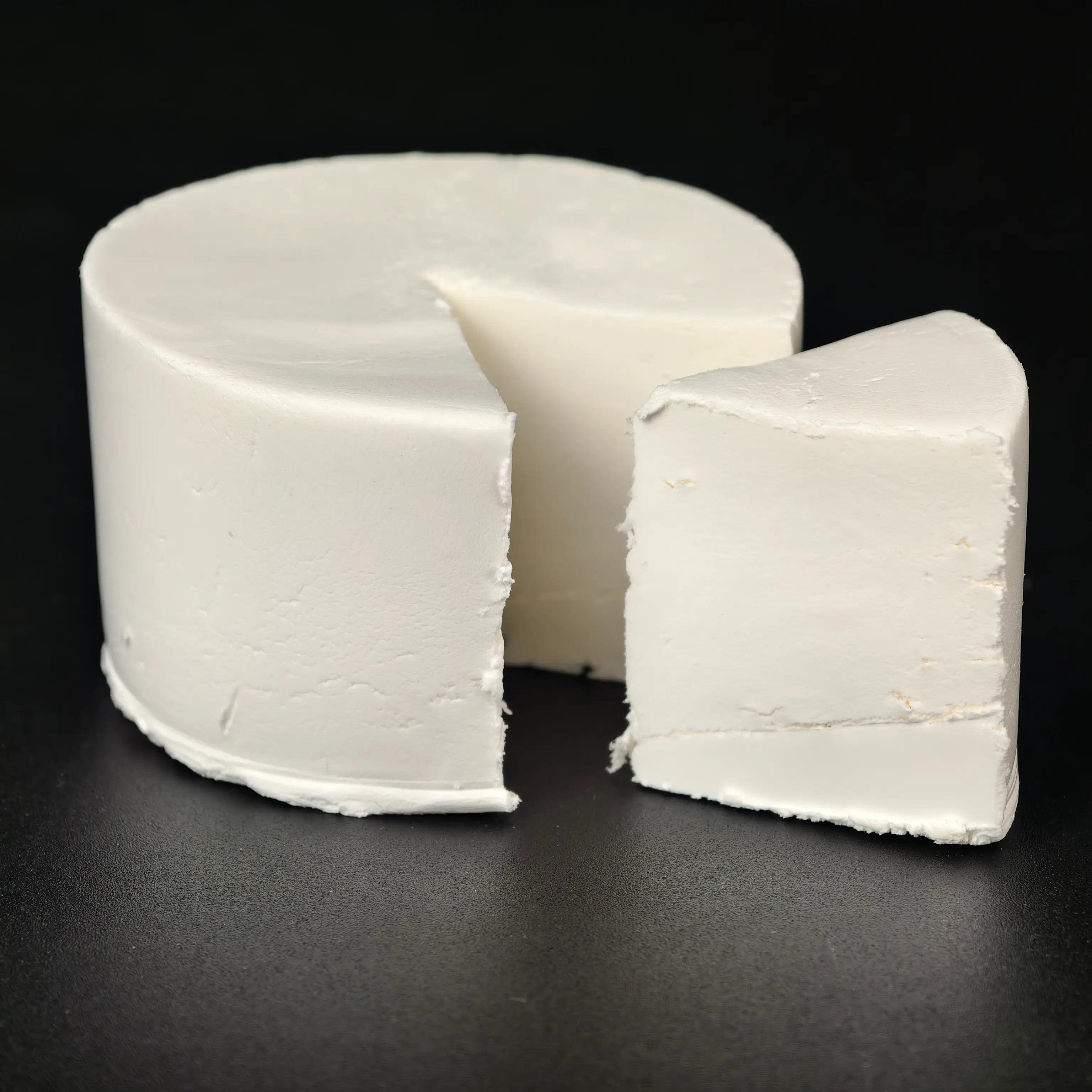 White creamy clay cheese wheel with a smooth, fine texture and a wedge cut out, set against a black background