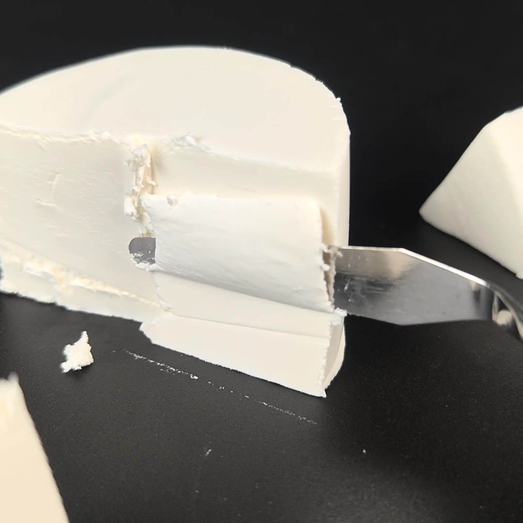 Smooth, white clay cheese wheel with a wafer-thin slice removed on black background.